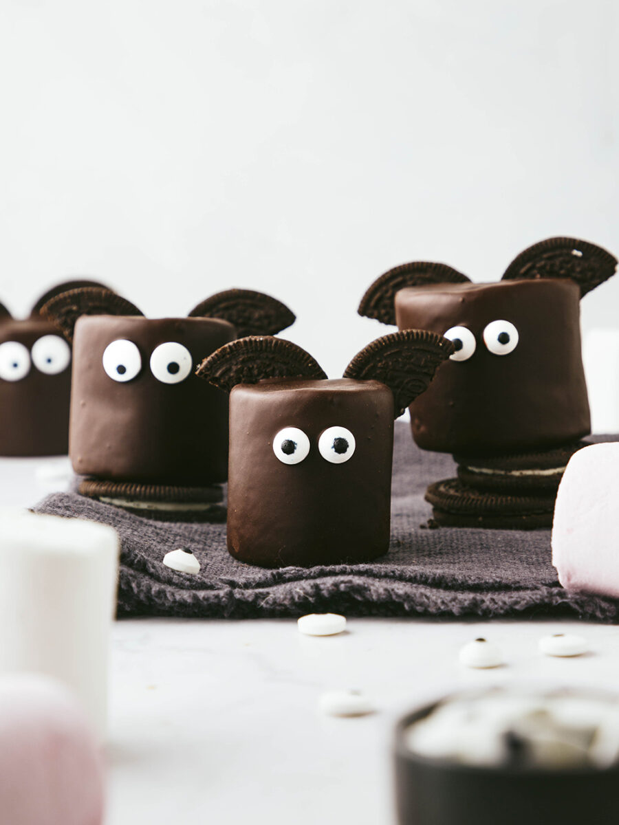 These marshmallow halloween bats are chocolate covered marshmallows with Oreo halves for wings and edible eyes sit on a dark grey fringed napkin against a light grey backdrop.
